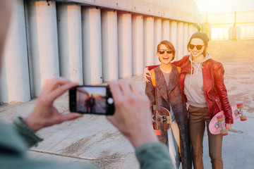 Man taking pictures of two young happy short-haired women with skateboards
