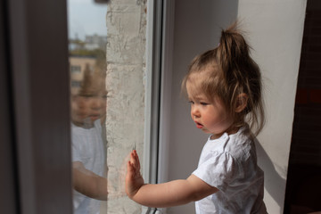 little girl looks out the window and asks outside during quarantine caused by coronavirus.