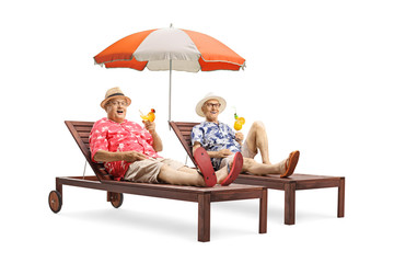Two senior male tourist with cocktails lying on sunbeds with an umbrella