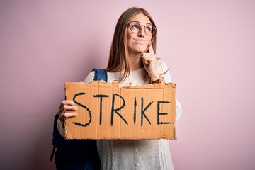 Young beautiful redhead activist woman holding banner with strike message serious face thinking...