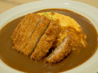 Curry Rice with Crispy Pork Cutlet and Omelette on wooden table.