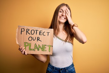 Young redhead woman asking for enviroment holding banner with protect planet message stressed with hand on head, shocked with shame and surprise face, angry and frustrated. Fear and upset for mistake.