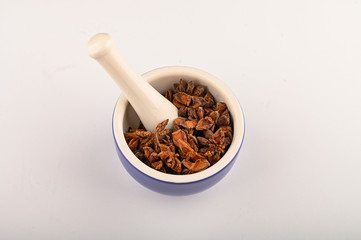 star anise in a blue ceramic spice mortar with a pestle on a white background. Close up.