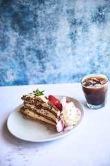 Glass of black ice coffee with slice of cake