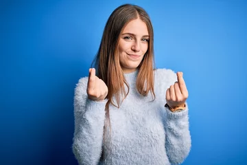 Fotobehang Young beautiful redhead woman wearing casual sweater over isolated blue background doing money gesture with hands, asking for salary payment, millionaire business © Krakenimages.com
