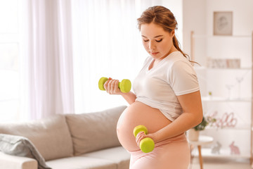 Sporty pregnant woman with dumbbells at home