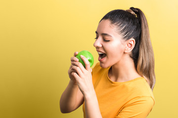 healthy lifestyle. starving girl on diet about to bite an apple with against yellow background