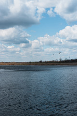 Beautiful spring cloudy sky, panorama, landscape. The lake and the snow-white clouds reflected in it. Haze in the blue sky and a beautiful blue river