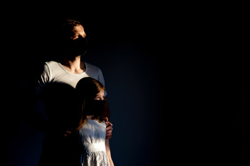 Dad and daughter, wearing black masks, stand by the virus and look out the window. bright light shines from the window, shooting in hard light.