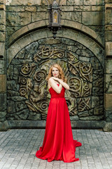 A woman in a red dress stands on a background of a medieval castle