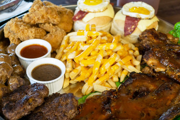 Close up of unhealthy food - steak, fried chicken, hamburger, ham, sauce, black pepper, french fries and meat ball on a big bowl.