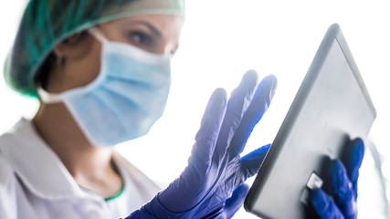 Cropped shot of an unrecognizable female nurse using a digital tablet while standing in a hospital....