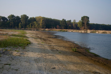 Blue river slow flowing across the green meadow and yellow sand with reflections of  trees in the water.  Fall