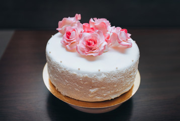 A single tier white wedding cake with pink rose flowers from a pastry glaze.