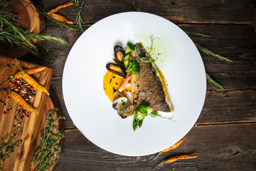 Top view on italian cuisine dish with fish fillet, mussels in sauce on a white plate on the wooden...
