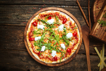 Top view on italian cuisine dish fresh cooked pizza with tomatoes, mozzarella cheese and arugula on the dark wooden table, horizontal format