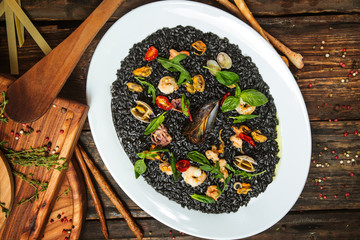Top view on italian cuisine dish black risotto with seafood on the white plate on the dark wooden table, horizontal format