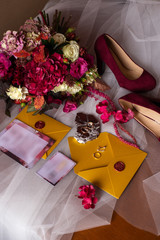 wedding accessories: a bride’s bouquet of roses, peonies and hydrangeas, wedding rings on a stone, a ring and earrings with diamonds, women's shoes, invitation and yellow envelopes with a red wax seal