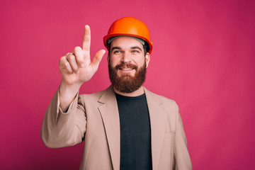 Portrait of happy architect pointing away and smiling over pink background, working time