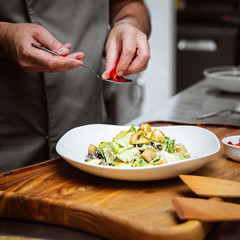 Restaurant chef cooking warm salad with lettuce, mushrooms and potato on the wooden board in the kitchen, square format