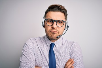 Young call center operator business man with blue eyes wearing glasses and headset skeptic and...