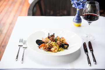 Closeup on appetizing italian cuisine restaurant  dish seafood pasta on the white table with a glass of red wine on the background, horizontal format