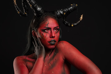young pretty girl doing body painting characterized by demon with big black horns and red and black...