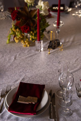 Place at the banquet table: a red napkin on plates pressed with a stone, cutlery and glasses on the sides of the plates, red candles, flower arrangement