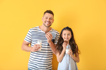Naklejka premium Father and daughter drinking milk with cookies on color background
