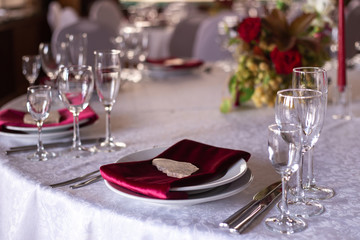 Place at the banquet table: a red napkin on plates pressed with a stone, cutlery and glasses on the sides of the plates, red candles, flower arrangement