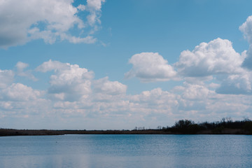 Beautiful spring cloudy sky, panorama, landscape. The lake and the snow-white clouds reflected in it. Haze in the blue sky and a beautiful blue river