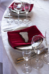 Place at the banquet table: a red napkin on plates is pressed by a stone, cutlery and glasses on the sides of plates