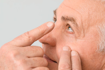 Obraz premium Mature man putting in contact lenses against light background