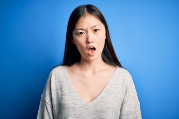Young beautiful asian woman wearing casual sweater standing over blue isolated background In shock face, looking skeptical and sarcastic, surprised with open mouth