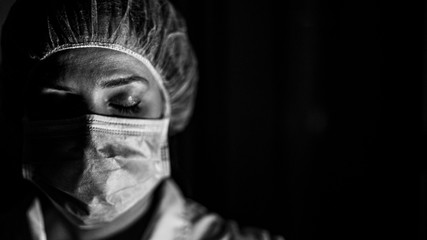Portrait black and white of young female surgeon, wearing mask and a surgical mask, in front of black background