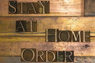 Photo of real authentic typeset letters forming Stay At Home Order text on vintage textured grunge copper background