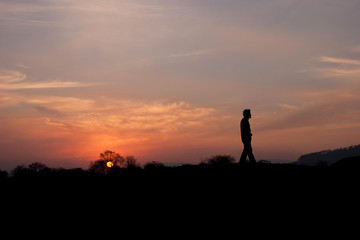 man walks alone in landscape at sunset backlit