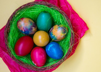 Green grass nest in a basket with colored chicken Easter eggs, multicolored painted eggs, Easter tradition, celebration concept 