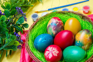 Green grass nest in a basket with colored chicken Easter eggs, multicolored painted eggs,paints and plastic flowers, Easter tradition, celebration concept 