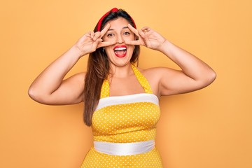 Young hispanic pin up woman wearing fashion sexy 50s style over yellow background Doing peace symbol with fingers over face, smiling cheerful showing victory