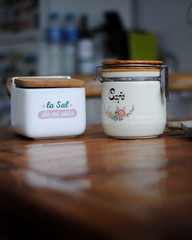 Dos bols de color blanco con la tapa de madera encima de una mesa también de madera. Un bol...