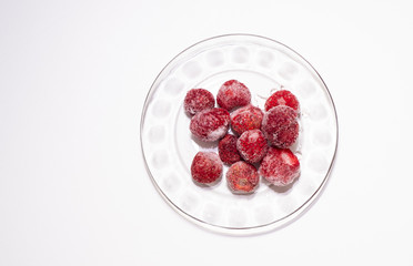 Frozen strawberries on a glass saucer and a white background.