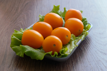 Yellow cherry tomatoes on a lettuce lie on a plate. Plate is on a wooden tabletop.