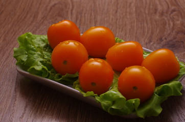 Yellow cherry tomatoes covered with drops of water on a lettuce leaf lie on a plate. Plate is on a wooden tabletop.
