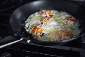 Fried eggs sprinkled with cheese lie in a hot pan