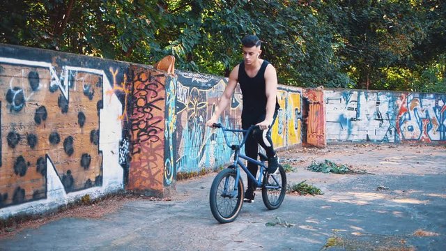 Young teenager rides and then pulls up a BMX bike. Copy space. Slowmo. Slow motion. Crop. 4K.