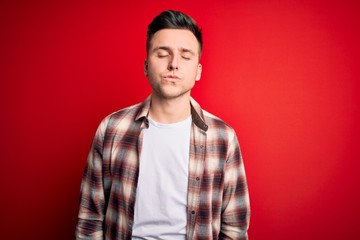 Fototapeta premium Young handsome caucasian man wearing casual modern shirt over red isolated background looking at the camera blowing a kiss on air being lovely and sexy. Love expression.