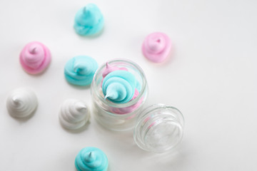 Colorful tasty meringues cookies in glass jars on white table background