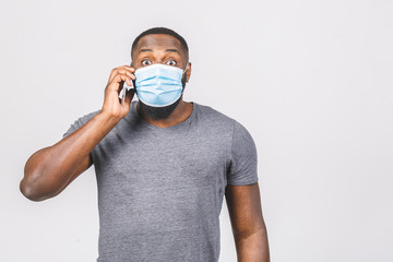 Shocked young african american man in sterile face mask posing isolated on white wall background....