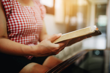 Close up of a woman sitting on the sofa and reading bible or book at home with window light